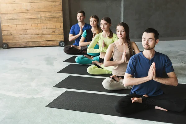 Jovens mulheres e homens na aula de ioga, relaxe a postura de meditação — Fotografia de Stock