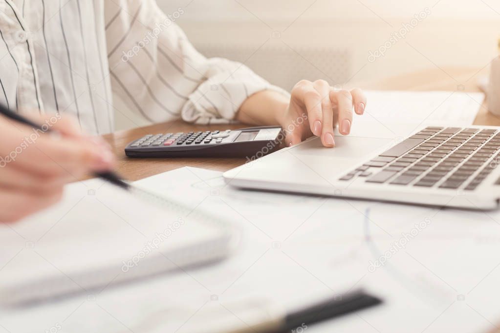 Closeup of woman hands typing on laptop and counting on calculator