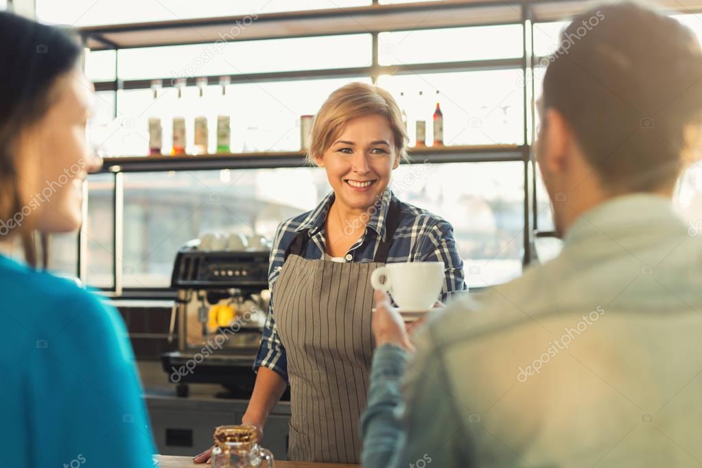 Experienced smiling barista making coffee to customers