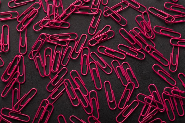 Pilha de clipes de papel rosa na mesa preta, material de escritório fundo — Fotografia de Stock