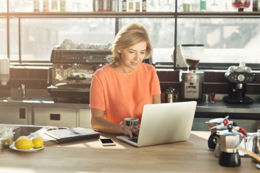 Dizüstü bilgisayarda çalışan mutlu orta yaşlı bir kadın barista