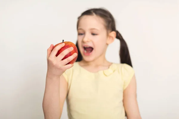 Досить мила дівчинка кусає червоне яблуко на білому тлі — стокове фото