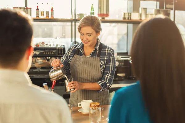 Experienced smiling barista making coffee to customers