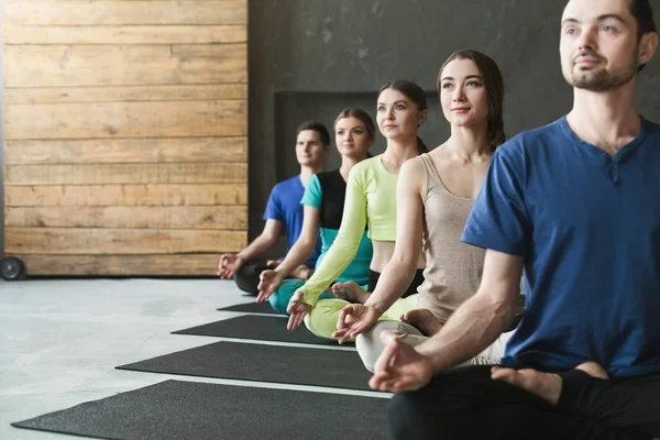 Giovani donne e uomini in classe di yoga, rilassarsi posa meditazione — Foto Stock