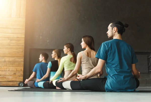 Mujeres jóvenes y hombres en clase de yoga, relajar la meditación pose — Foto de Stock