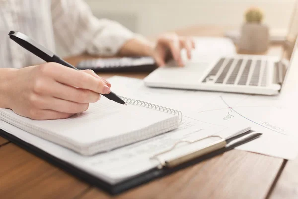 Primer plano de las manos de la mujer escribiendo en el ordenador portátil y contando con la calculadora —  Fotos de Stock