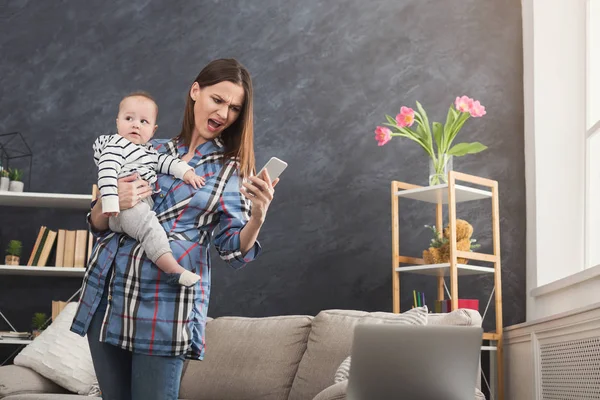 Boze moeder bedrijf baby tijdens het gebruik van de telefoon — Stockfoto