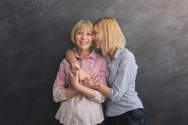 Feliz madre adulta e hija abrazando sobre fondo gris — Foto de Stock