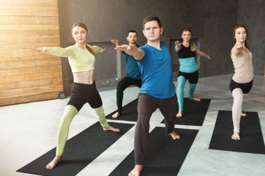 Genç kadın ve erkekler yoga sınıfındaki germe egzersizleri yapıyor