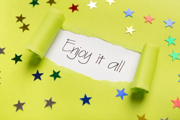 Enjoy it all phrase showing up under torn yellow paper — Stock Photo, Image