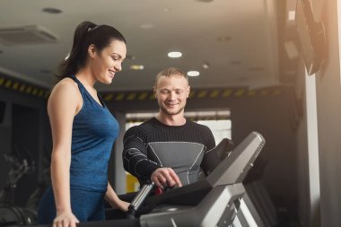 Spor hocası eliptik eğitmen kadına yardımcı olur.