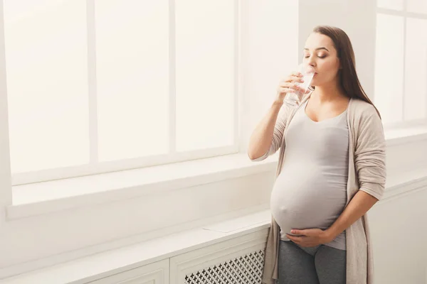 Těhotná žena pitné vody na okně — Stock fotografie