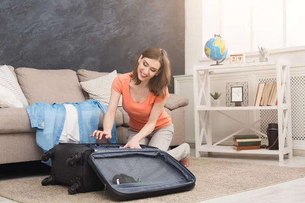 Happy woman packing clothes into travel bag