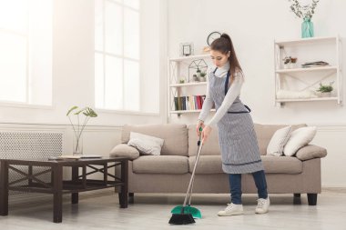 Genç kadın süpürge ve kepçe ile ev süpürme