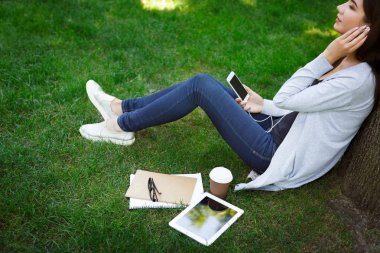 Genç kadın Asyalı gülümseyen bu öğrenci kulaklık. Müzik ve parkta kahve içme