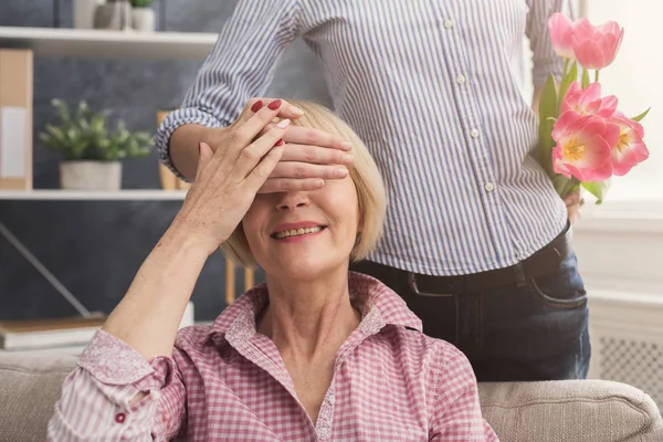 Tochter schließt Mutter die Augen und schenkt Blumen — Stockfoto