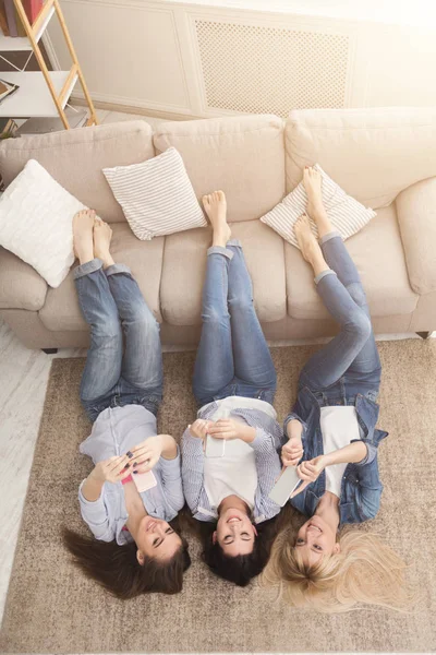 Счастливые девочки, лежащие на полу и пользующиеся смартфонами, вид сверху — стоковое фото