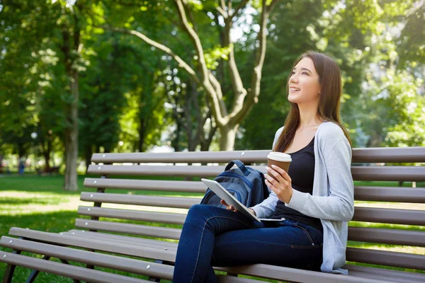 Motivado freelancer asiático en el parque. Chica en un banco, beber café y trabajar con la tableta — Foto de Stock