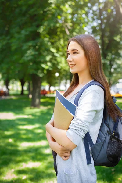 Молодая азиатская студентка, с книгами и рюкзаком. Оставаться в парке и улыбаться — стоковое фото