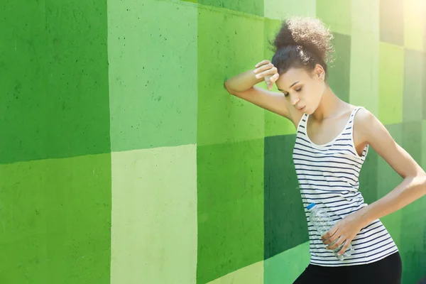 Tired woman runner is having break, leaning on green wall — Stock Photo, Image