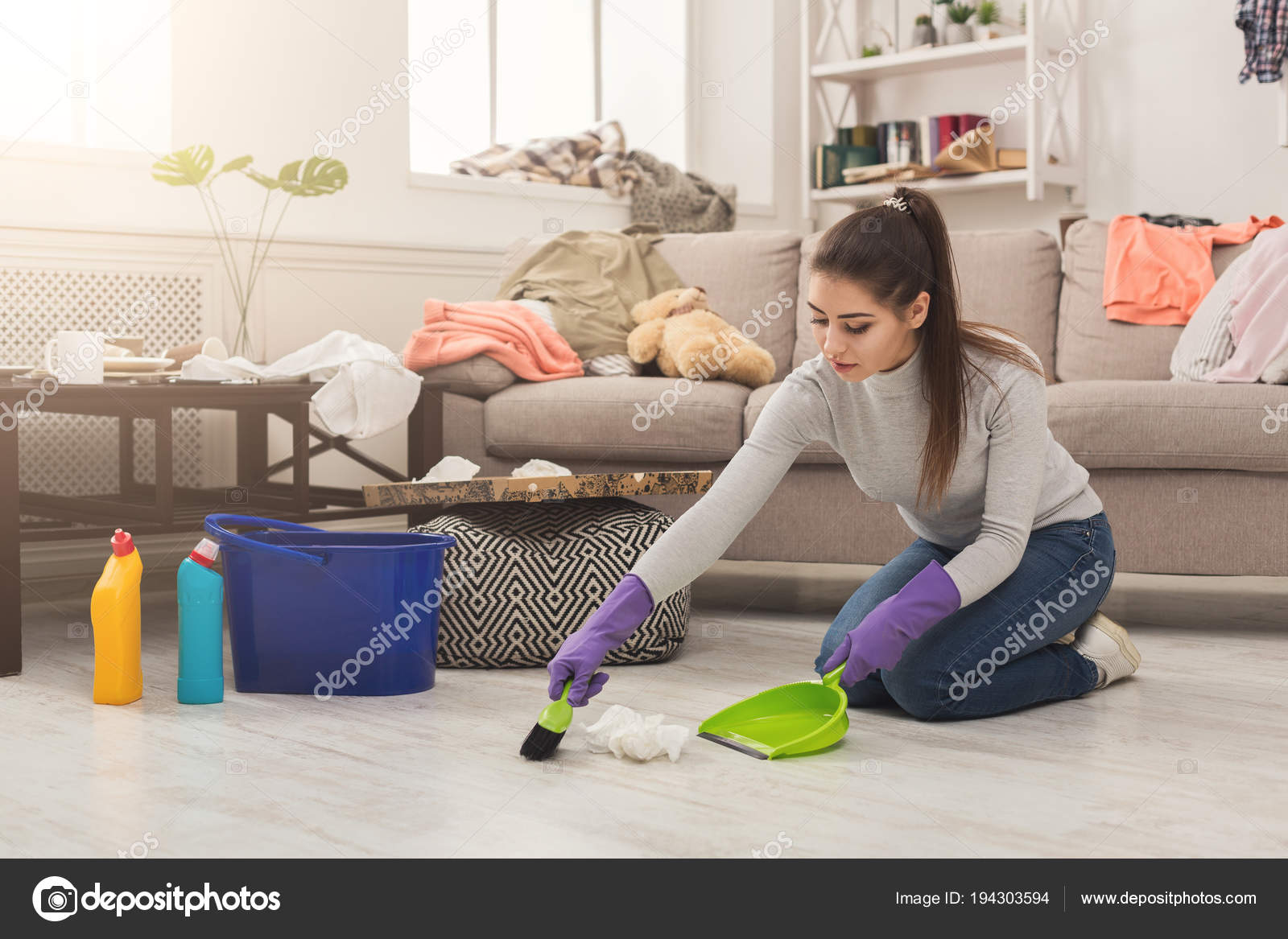 Young Woman Sweeping Floor In Messy Room Stock Photo