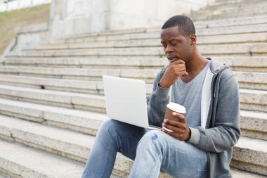 Dalgın siyah adam açık havada dizüstü bilgisayar kullanarak