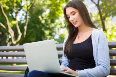 Parkta motive serbest meslek. Bir bankta kız gülümseyerek ve laptop ile çalışma
