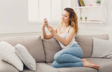 Kanepenin üzerinde cep telefonu kullanan genç kız