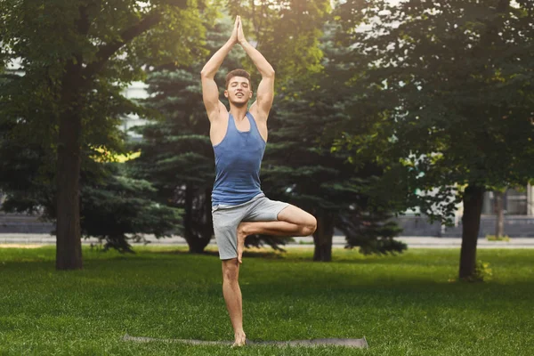Ung man utbildning yoga i tree pose utomhus — Stockfoto