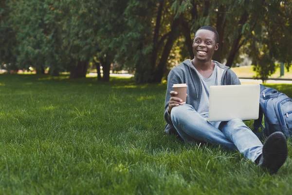Χαμογελώντας φοιτητής κάθεται στο γρασίδι, χρησιμοποιώντας φορητό υπολογιστή — Φωτογραφία Αρχείου