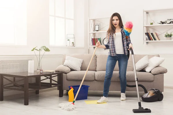 Geschokt vrouw reinigen van huis met tal van instrumenten — Stockfoto