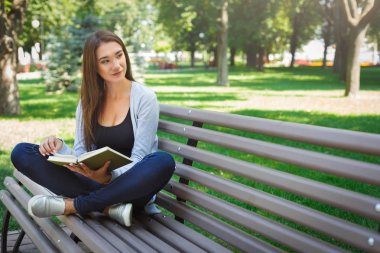 Genç Asyalı kadın parkta bir bankta oturmuş. Rahatlatıcı ve bir kitap okuma