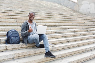 Gülümseyen öğrenci dizüstü kullanarak merdivenlerde oturan