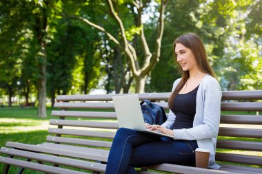 Parkta motive serbest meslek. Bir bankta, kahve içme ve laptop ile çalışan kız