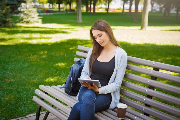 Motivované asijské na volné noze v parku. Dívka na lavičce, popíjel kávu a práce s tabletem — Stock fotografie