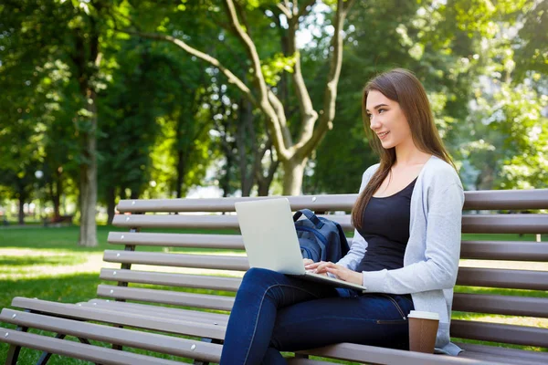 公園では独創力のある、フリーランス。女の子、ベンチでコーヒーを飲みながら、ノート パソコンでの作業 — ストック写真