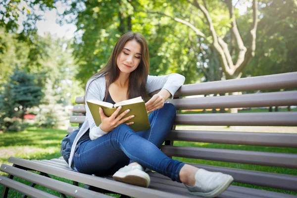 Молода азіатка сидить на лавці в парку. Розслабляючись і читаючи книгу — стокове фото