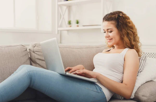 Chica joven con el ordenador portátil sentado en el sofá beige — Foto de Stock