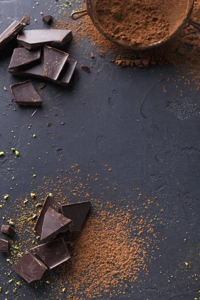 Dark chocolate pieces and cocoa powder over black background — Stock Photo, Image