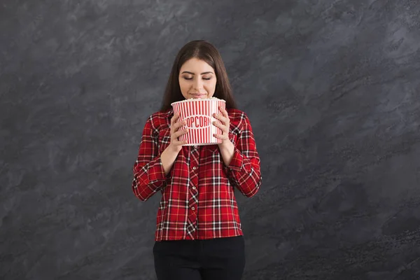 Happy beautiful young girl smelling popcorns on grey background — Stock Photo, Image