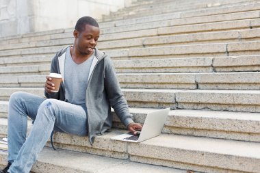 Gülümseyen öğrenci dizüstü kullanarak merdivenlerde oturan