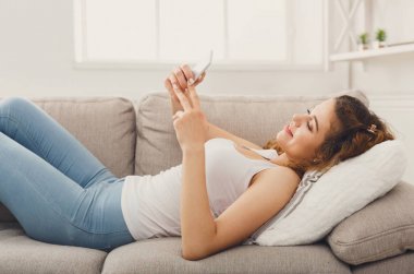 Kanepenin üzerinde cep telefonu kullanan genç Kızıl saçlı kız