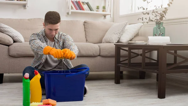 Уставший мужчина убирает дома с помощью моющих средств — стоковое фото