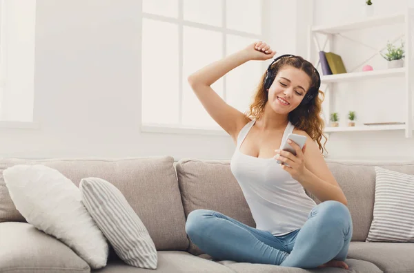 Gelukkig jonge vrouw in de koptelefoon op beige couch — Stockfoto