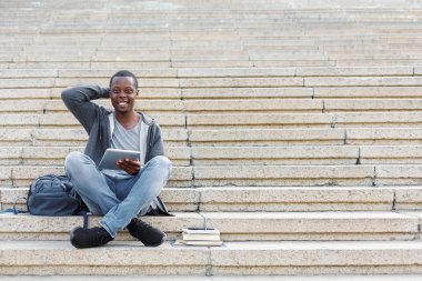 Gülümseyen öğrenci tablet kullanarak merdivenlerde oturan