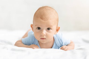 Sevimli bebek karnının üstünde yatakta yatıyor.