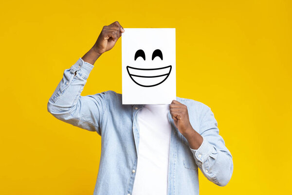 African man hiding face behind paper with drawn happy emoticon