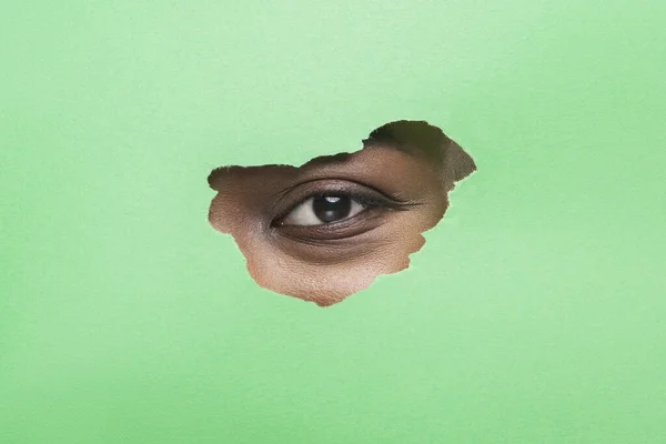 Zwarte vrouwen oog zonder Mascara Kijken door gescheurd Groenboek — Stockfoto