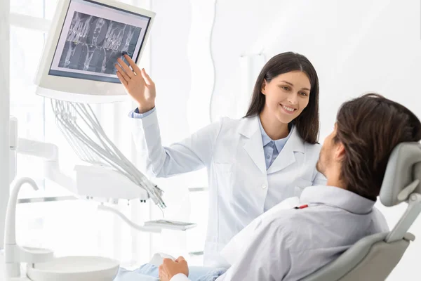 Kaunis naispuolinen hammaslääkäri, joka näyttää potilaan röntgentulokset — kuvapankkivalokuva