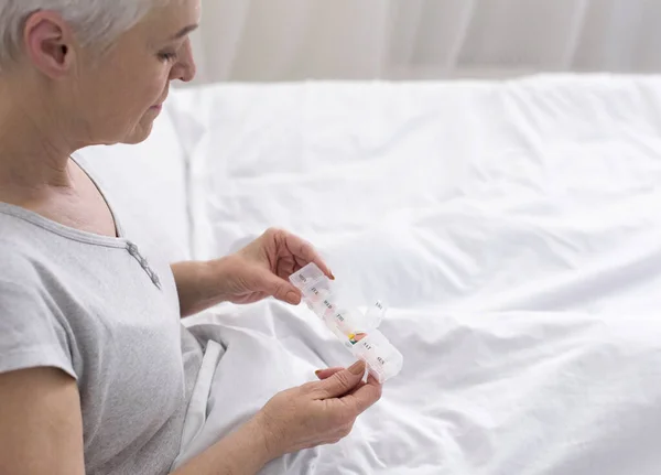 Señora mayor tomando pastillas de la caja médica, sentada en la cama — Foto de Stock